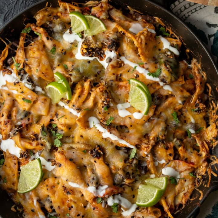 chicken fajita casserole in a cast iron skillet topped with Mexican crema, limes, cilantro, and hot sauce