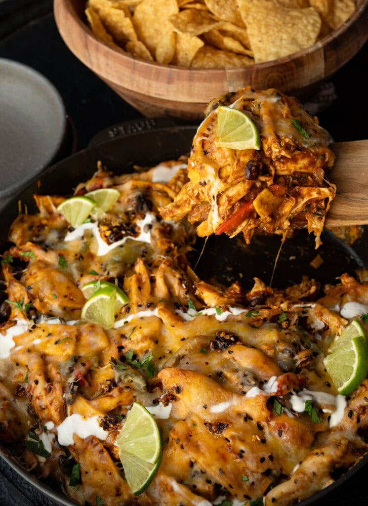 serving the casserole with a wooden spatula next to a bowl of tortilla chips