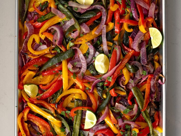 roasted fajita veggies on a half sheet pan garnished with cilantro and lime wedges