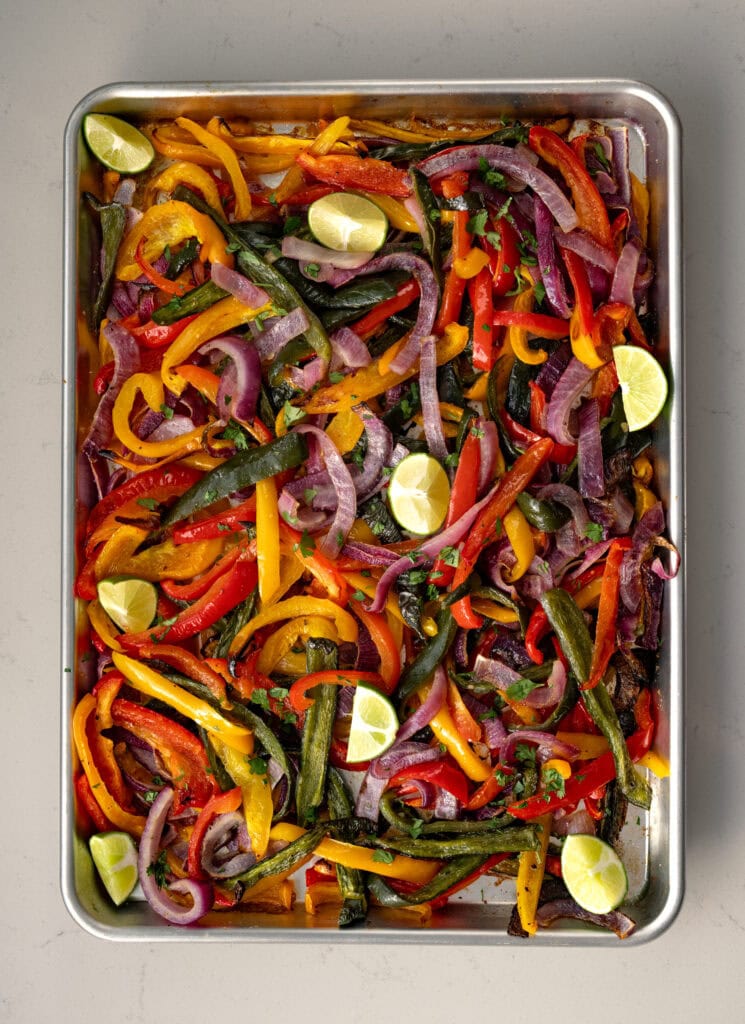 roasted fajita veggies on a half sheet pan garnished with cilantro and lime wedges