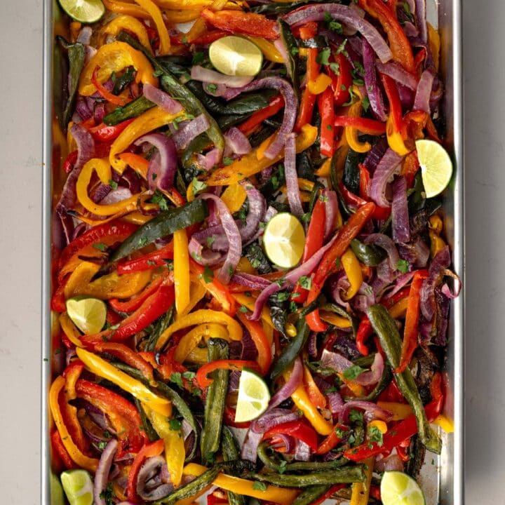 roasted fajita veggies on a half sheet pan garnished with cilantro and lime wedges