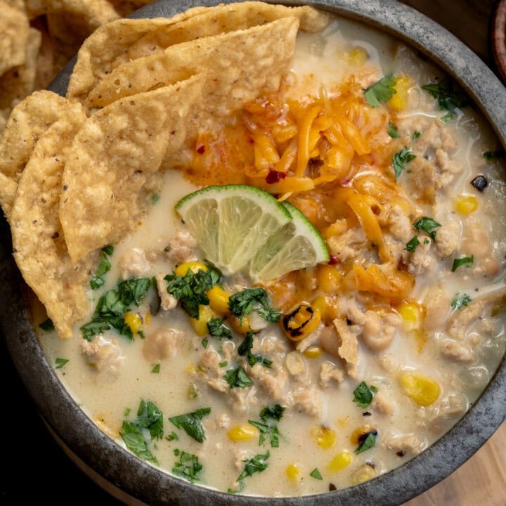 white chicken chili in a bowl with tortilla chips, lime wedges, shredded cheddar cheese, and chopped cilantro