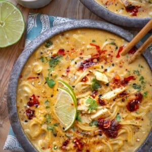 bowl of Thai yellow curry chicken ramen soup garnished with lime wedges and chili crisp