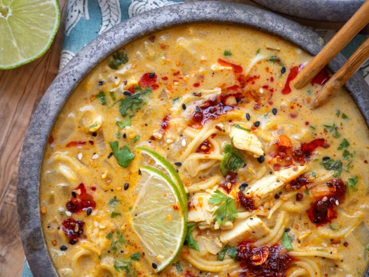 bowl of Thai yellow curry chicken ramen soup garnished with lime wedges and chili crisp