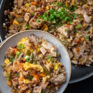 holding a bowl of rotisserie chicken fried rice garnished with scallions and chili crisp