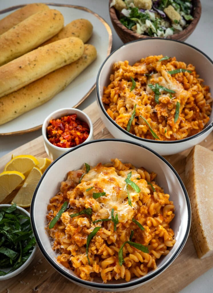 two bowls of ground chicken Goodles with breadsticks and salad