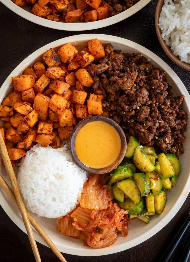 gochugaru roasted sweet potatoes and gochujang ground beef bowls with rice, kimchi, cucumber salad, and a creamy sauce