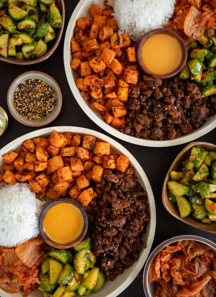 two gochujang ground beef and sweet potato bowls surrounded by banchan