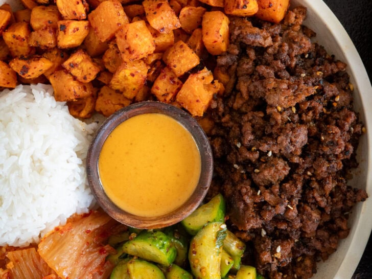 Korean inspired ground beef and sweet potatoes in a bowl with kimchi, pickled cucumbers, rice, and ssamjang mayo