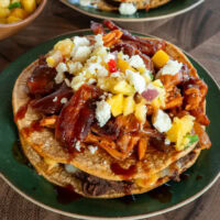 a double decker smoked bbq chicken tostada on a green plate topped with pineapple salsa