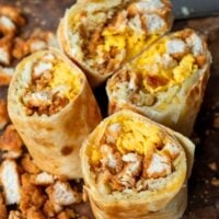 two large chicken and hash browns breakfast wraps sliced in half on a cutting board surrounded by chopped chicken breast bites