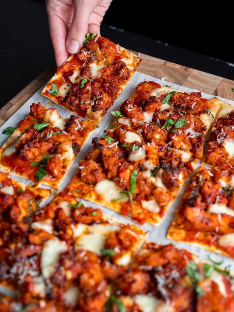 picking up a corner piece of a sliced chicken flatbread