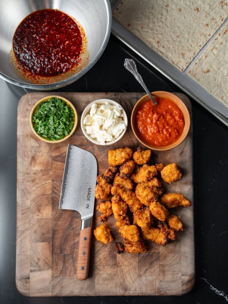 air fried chicken breast bites on a cutting board next to flatbreads on a sheet pan and bowls of marinara, fresh mozzarella, Calabrian chili sauce, and chopped basil