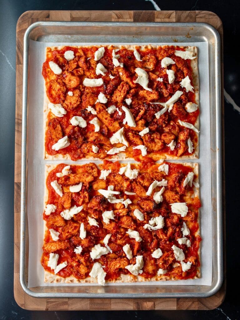 assembled Calabrian chicken flatbreads on a parchment lined half sheet pan before baking