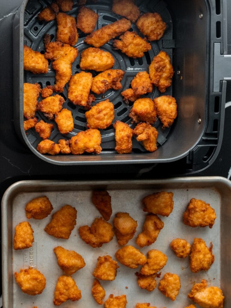 cooked frozen chicken bites in an air fryer basket and on a quarter sheet pan