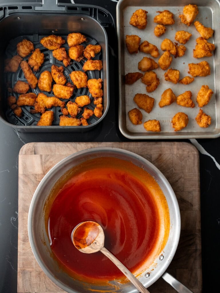 chicken bites in an air fryer basket and on a sheet pan next to a pan full of honey chipotle sauce