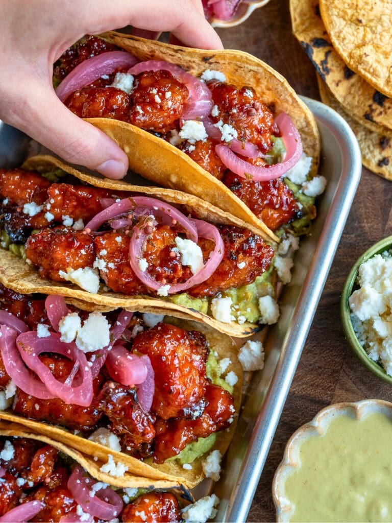 picking up a taco off the sheet pan with four chicken tacos