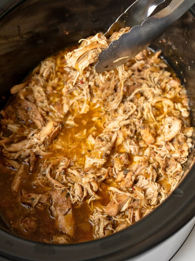 serving shredded chicken out of a Crockpot with tongs