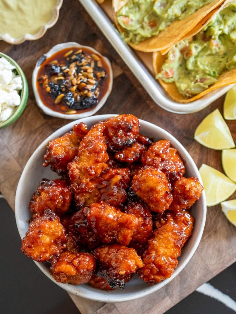 air fried honey chipotle chicken in a bowl next to corn tortillas filled with guacamole, lime wedges, salsa, macha, queso fresco, and salsa