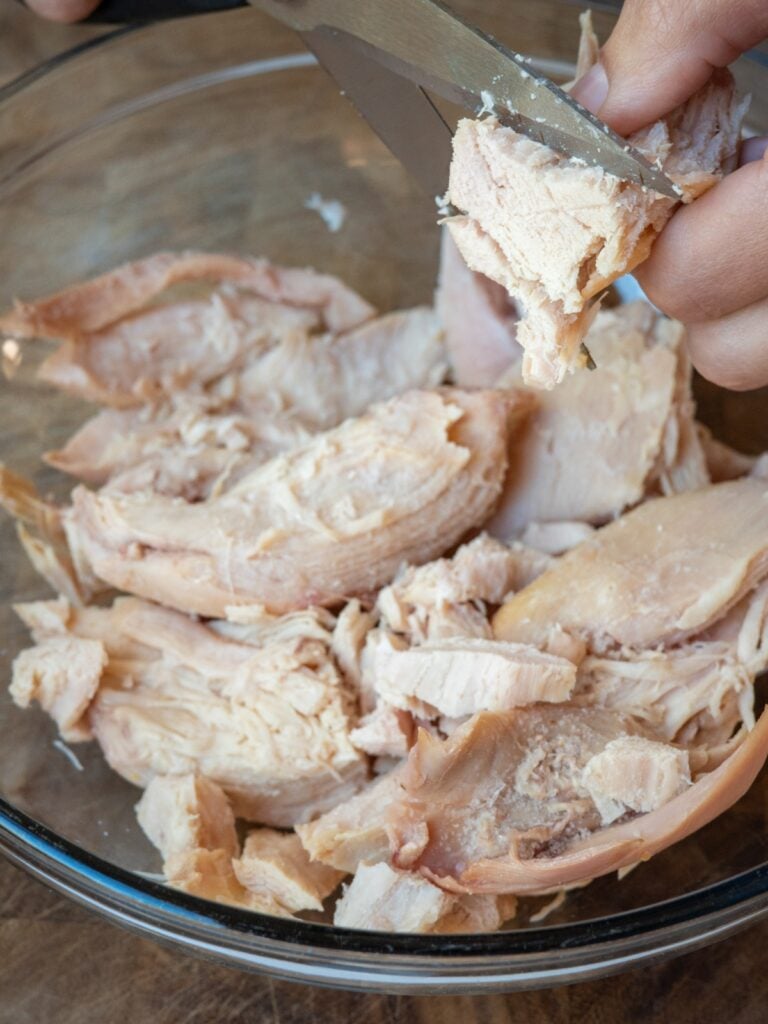 cutting pulled rotisserie chicken into bite size pieces with kitchen scissors