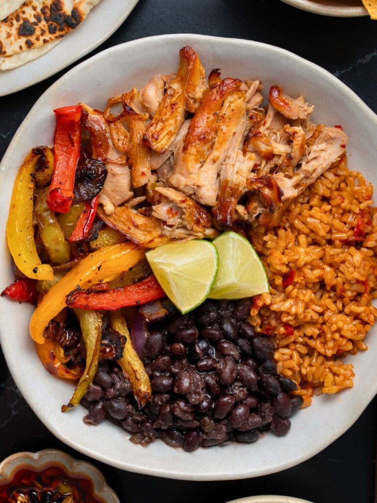 shredded Mexican chicken burrito bowl with fajita veggies, black beans, rice, and lime wedges