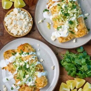 two plates with green chile rotisserie chicken enchiladas garnished with Greek yogurt, shredded lettuce, cilantro, and queso fresco