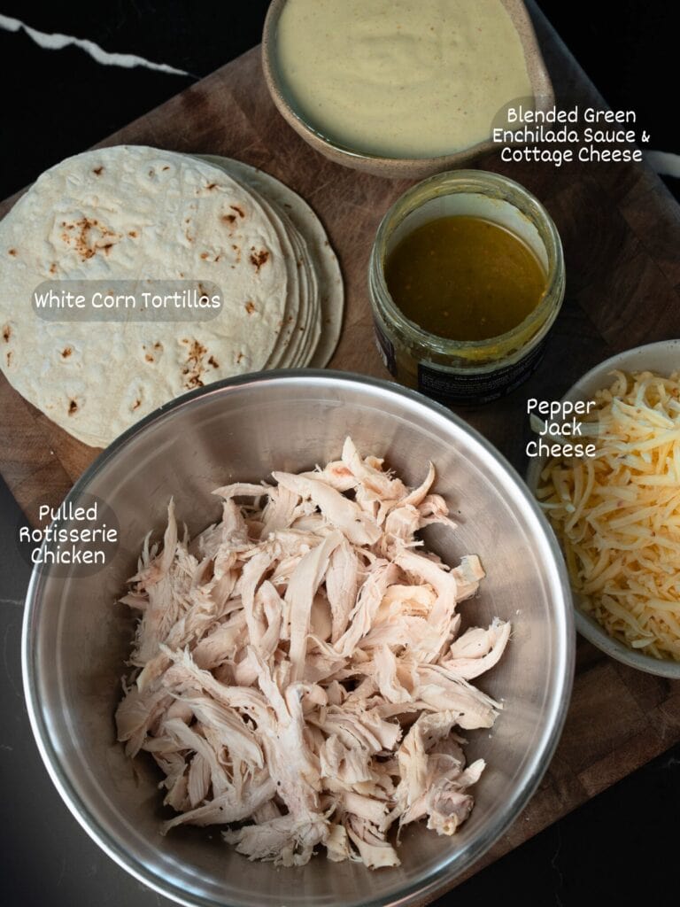 pulled rotisserie chicken, green enchilada sauce, blended cottage cheese enchilada sauce, shredded pepper jack, and corn tortillas on a cutting board