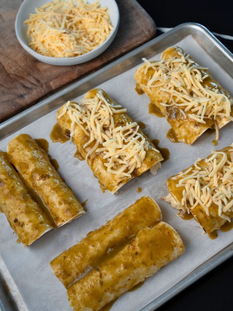 topping rolled enchiladas with enchilada sauce and shredded cheese