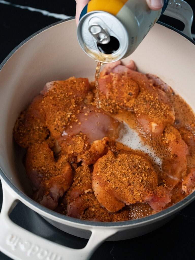 pouring beer in a Dutch oven with chicken thighs and seasoning