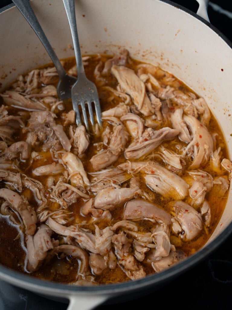 shredded chicken and two forks in a Dutch oven