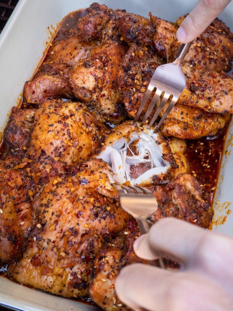 shredding smoked chicken thighs in a baking dish on a Traeger grill