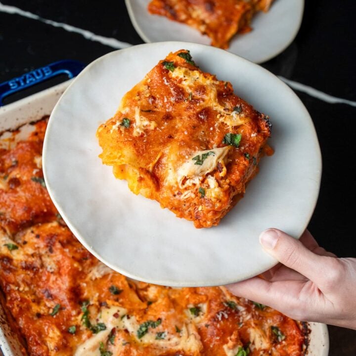 slices of rotisserie chicken lasagna on white plates next to a baking dish of lasagna
