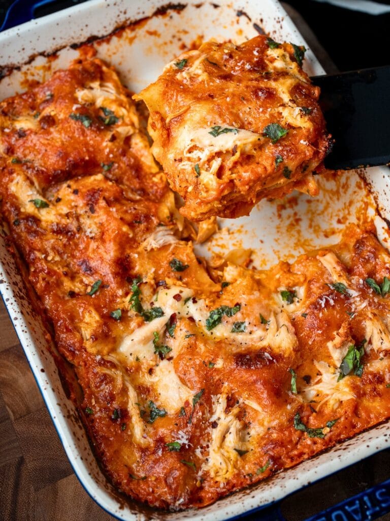serving a slice of chicken lasagna out of a baking dish with a black spatula