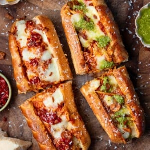 two rotisserie chicken sandwiches sliced in half on a cutting board and garnished with basil pesto and Calabrian chili peppers