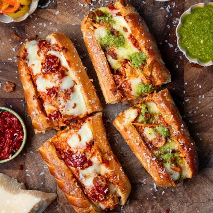two rotisserie chicken sandwiches sliced in half on a cutting board and garnished with basil pesto and Calabrian chili peppers