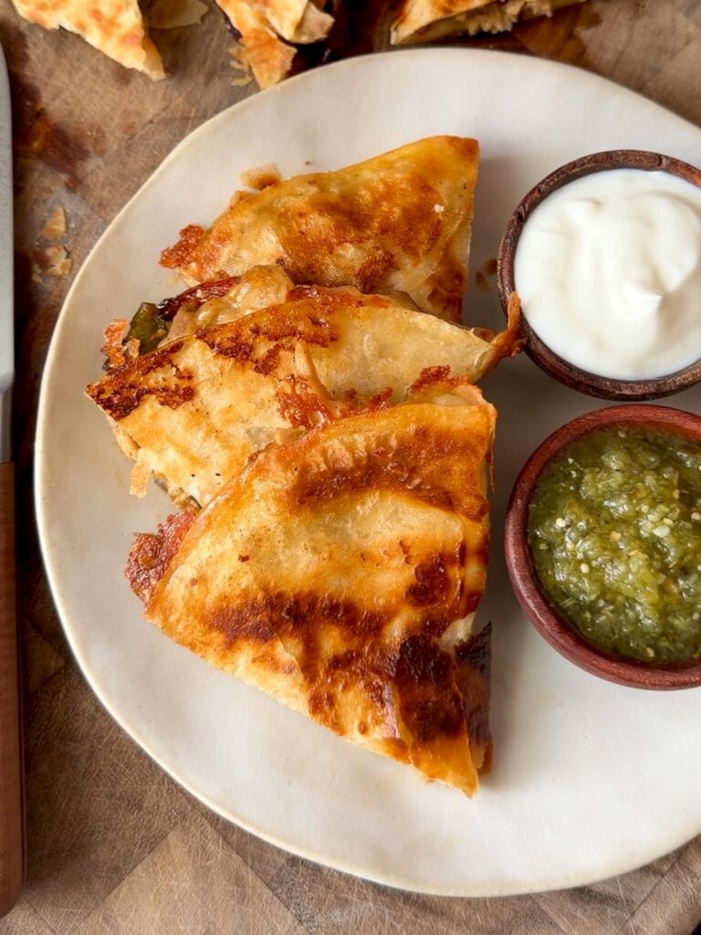Mexican chicken quesadilla cut into triangles on a plate with bowls of salsa verde and nonfat Greek yogurt