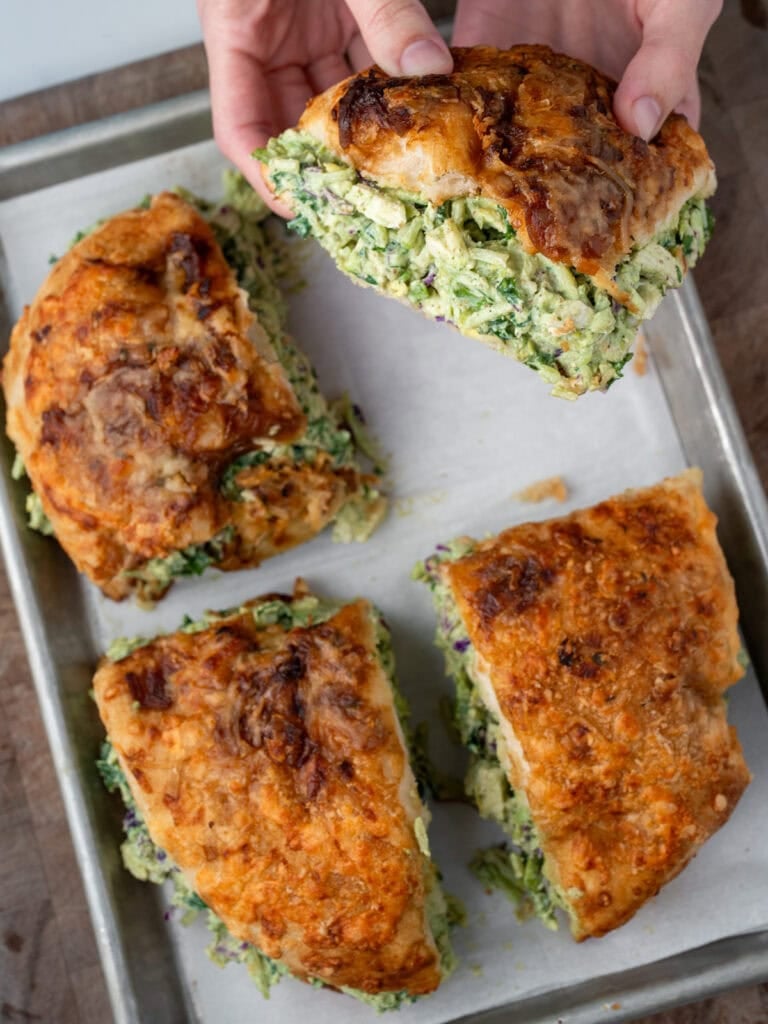 picking up one fourth of a pesto chicken salad focaccia sandwich off a sheet pan