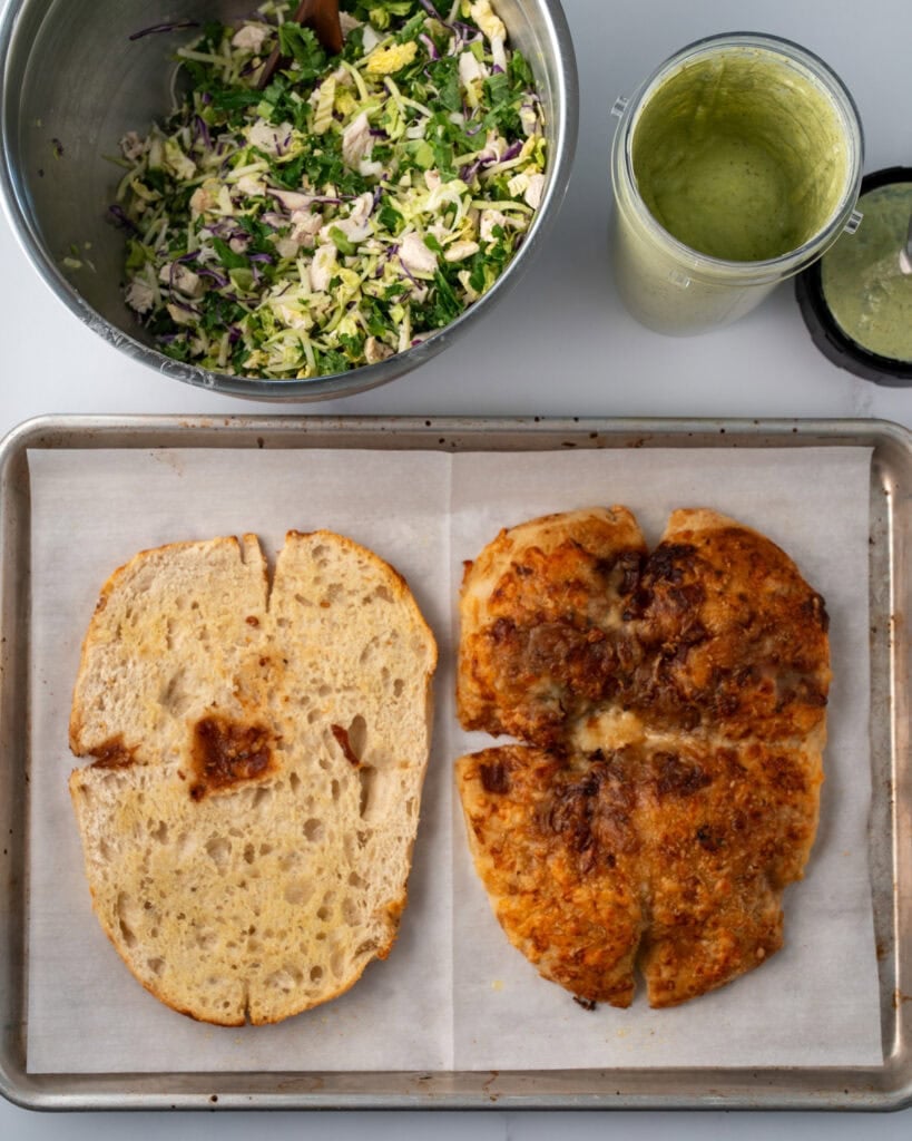 halved and baked focaccia on a sheet pan next to blended cottage cheese pesto and chopped chicken crunch salad