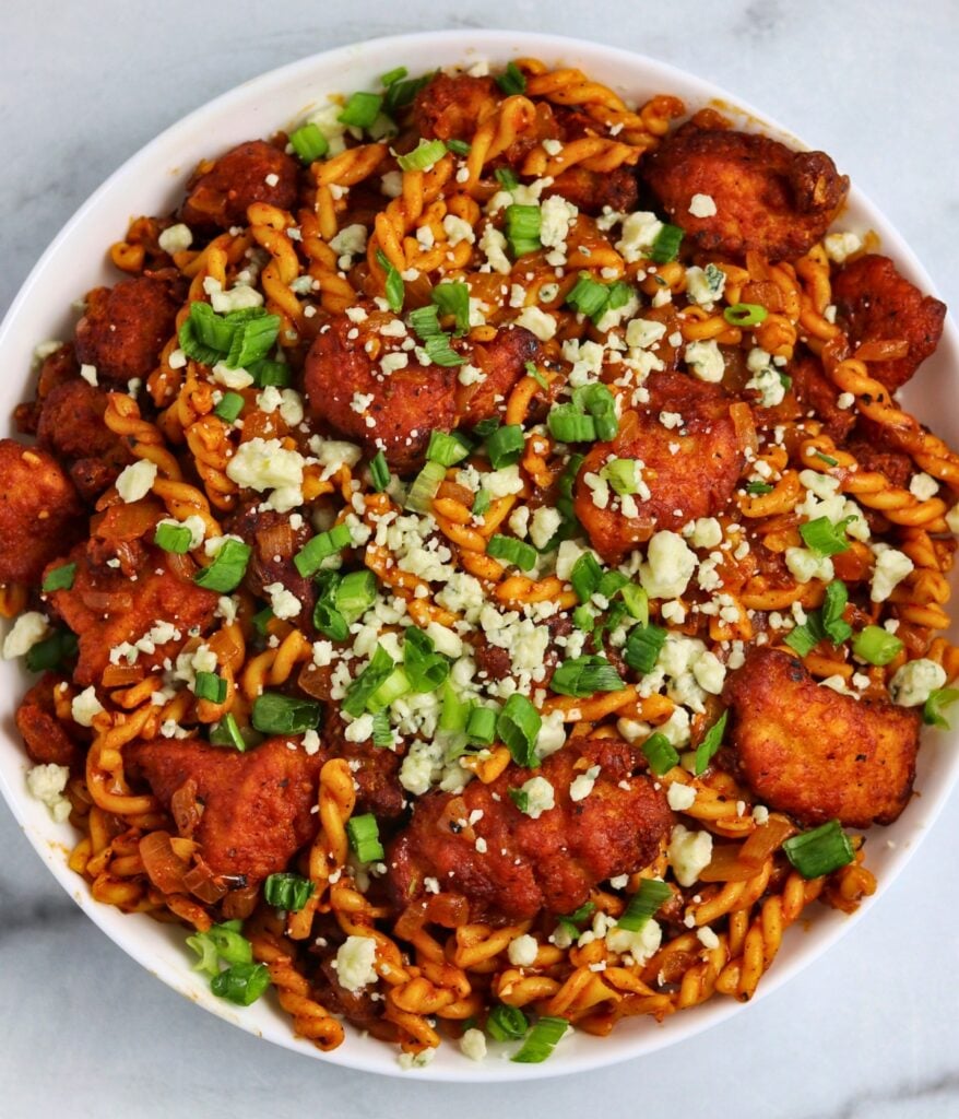 a bowl of buffalo chicken nuggets pasta topped with green onion and bleu cheese crumbles