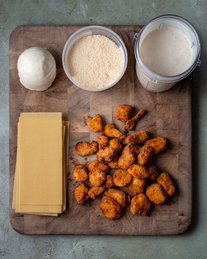 crispy chicken breast bites, lasagna sheets, fresh mozzarella, grated parmesan, and blended cottage cheese alfredo on a cutting board