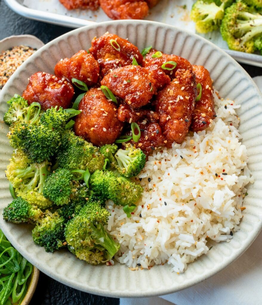 sheet pan baked chicken nuggets and broccoli florets with firecracker sauce in a rice bowl garnished with green onions