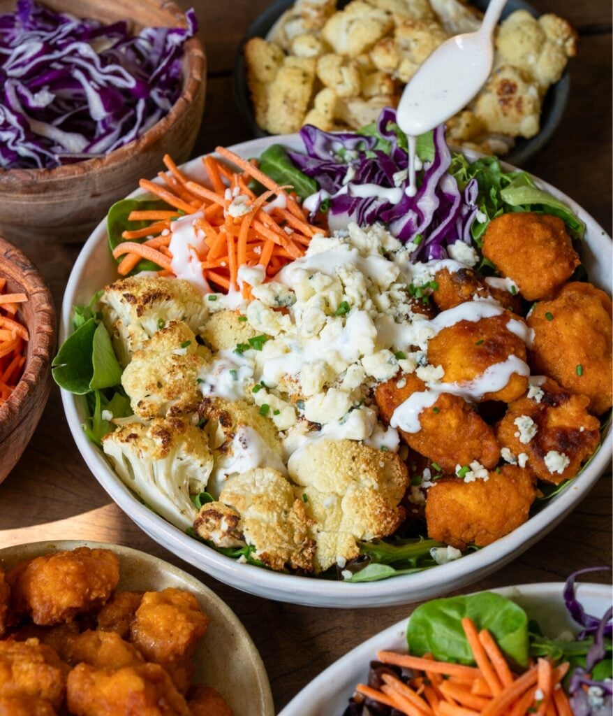 drizzling ranch over a buffalo chicken nuggets and roasted cauliflower power bowl
