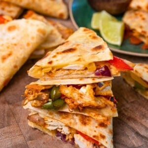 rotisserie chicken quesadilla triangles stacked on a cutting board with more quesadillas in the background
