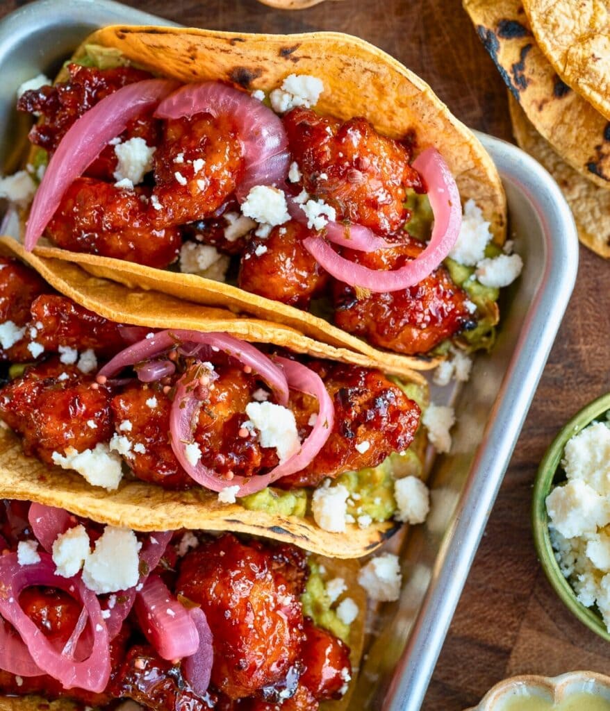 three chicken tacos on a sheet pan with guacamole, queso fresco, and pickled onions