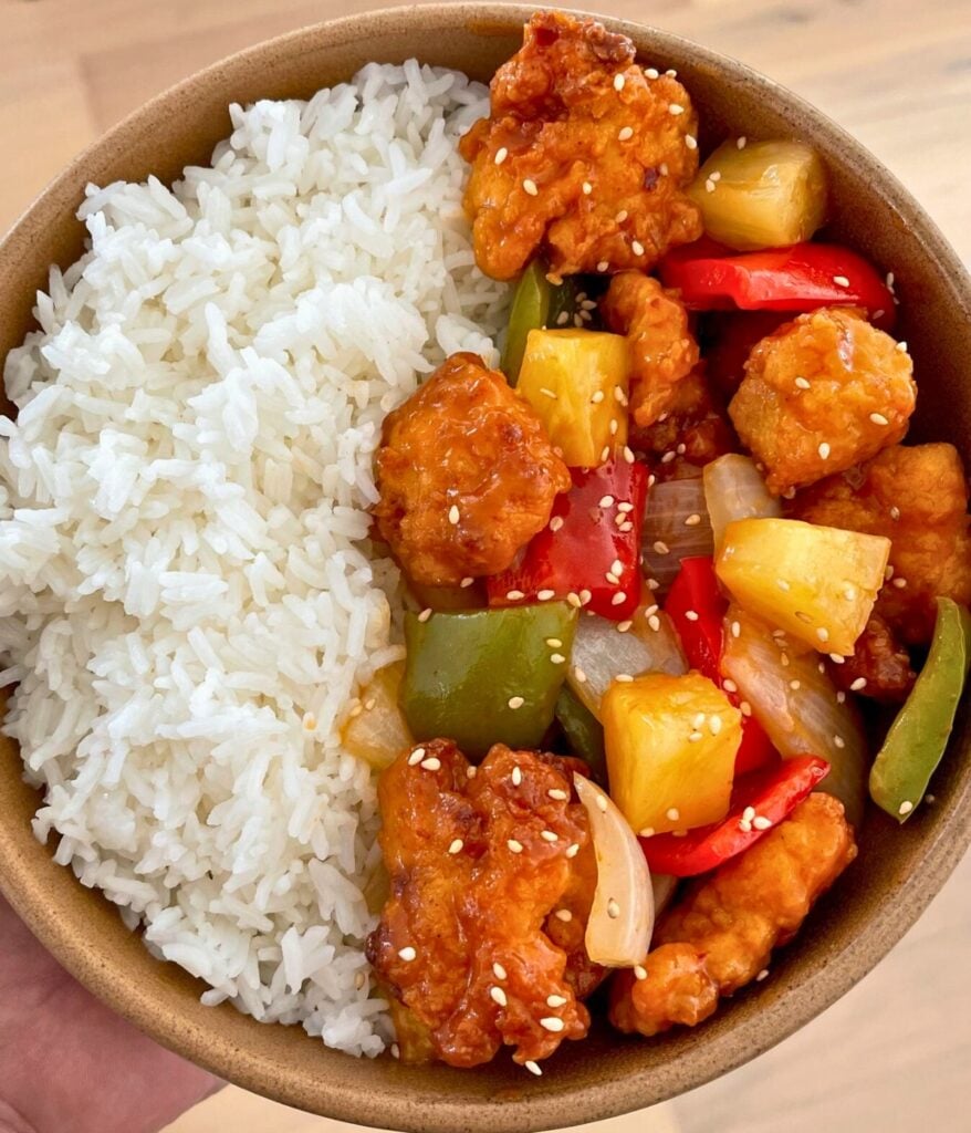 holding a rice bowl with sweet n sour chicken nuggets