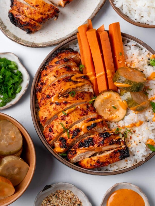 sliced Korean chile chicken breast in a rice bowl with pickled carrots and kimchi pickles