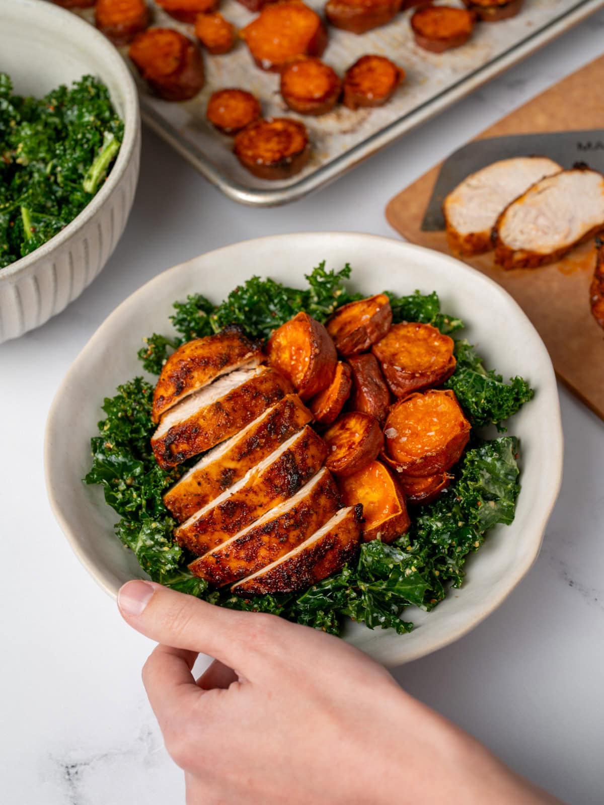 sliced bbq chicken breast in a bowl with kale salad and roasted sweet potatoes