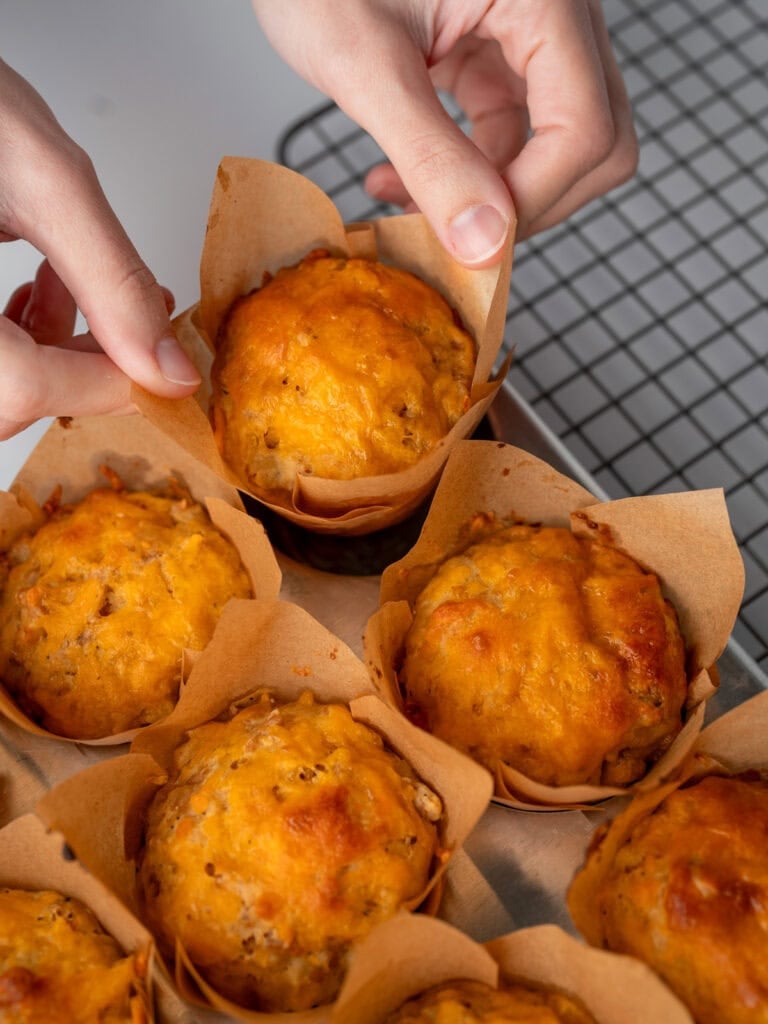 transferring a baked breakfast sausage muffin out of a muffin tin to a wire cooling rack