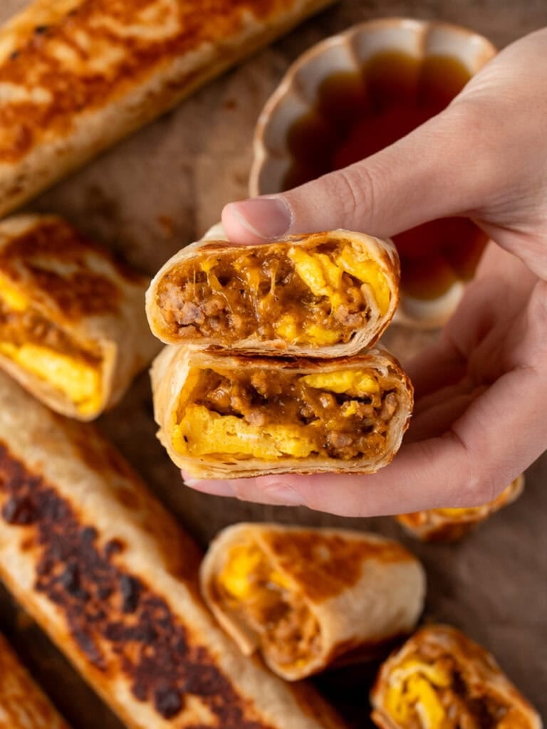 holding a sliced sausage egg and cheese roll-up 
