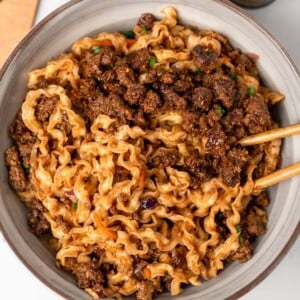 chopsticks in a bowl of noodles with crispy ground beef, saut&eacute;ed coleslaw mix, and a hoisin sauce